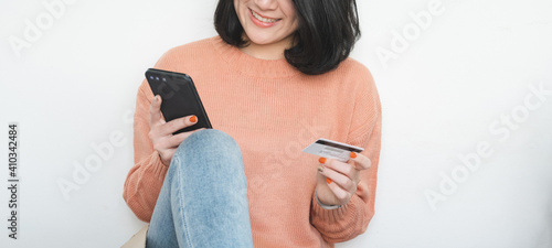 young woman sit on floor, using mobile phone, and holding credit card for online shopping