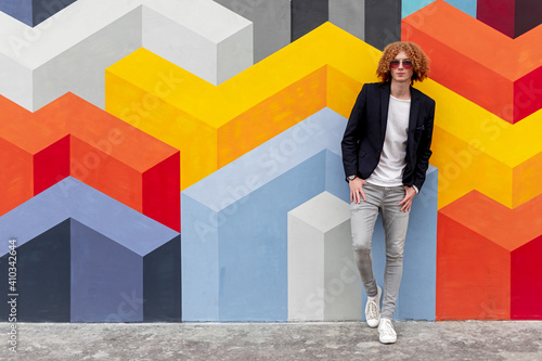 Trendy millennial ginger man in stylish wear standing near colorful wall