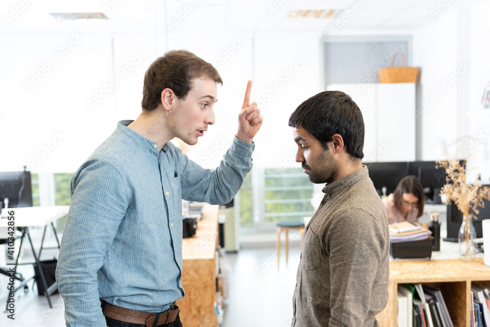 Obraz premium Handsome young man threatening his sad hispanic coworker at the office.