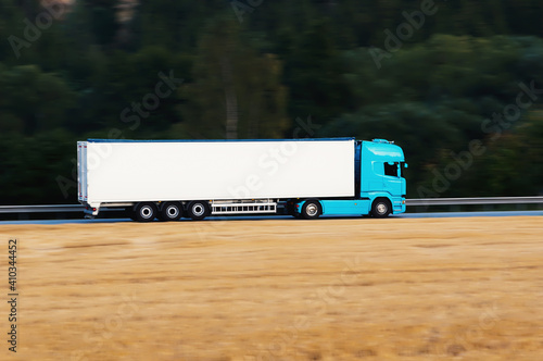 A blue truck driving on an asphalt road behind a yellow field