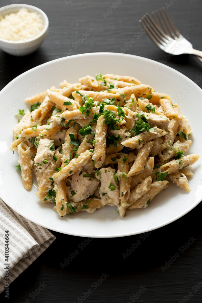 Homemade Chicken Alfredo Penne with Parsley on a black background, side view.