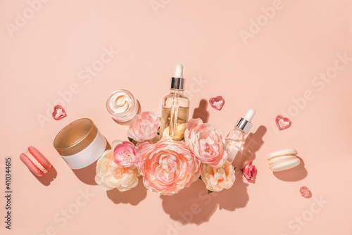 Natural cosmetics, bio serum and herbal oils and cream for spa and skin care in a composition with flowers. Trendy monochrome pastel background, flat lay. Natural skincare and perfume concept
