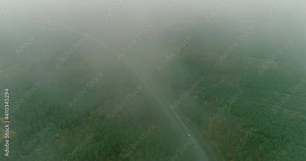 Drone landscape view. Misty countryside. Nature scenery. Cloudy day. Park panorama. Tree crowns and long asphalted road in fog daylight slow motion. Drone landscape view. Misty countryside. Nature scenery. Cloudy day. Park panorama. Tree crowns and long asphalted road in fog daylight slow motion.