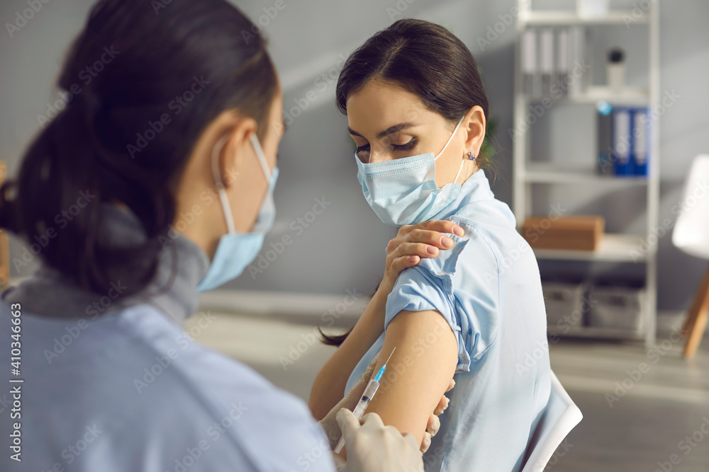 Vaccination and immunization concept. Doctor or nurse giving influenza shot to female patient. Young woman in medical face mask getting modern Covid-19 vaccine injection during infection outbreak
