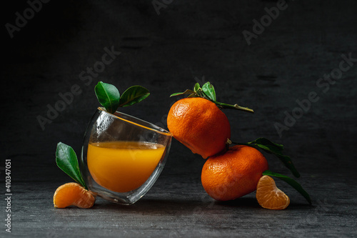 Glass of juice with tangerines on a black background. Trending style Balance and levitation. Fresh mandarin