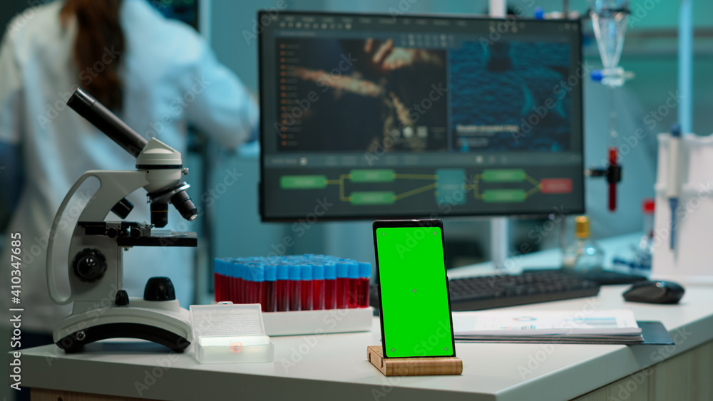 Smartphone with green screen working in laboratory with mock up, chroma key display while professional engineer testing virus evolution in background. High tech development lab with blood samples