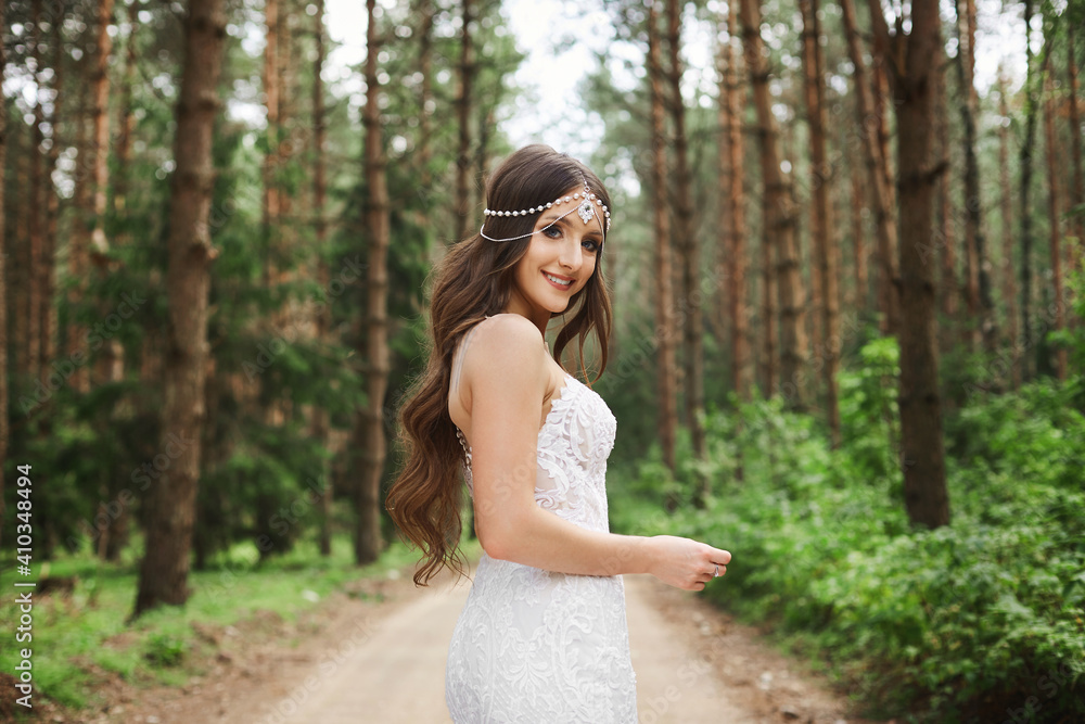 Beautiful young bride with wedding hairstyle with jewelry in lace dress holding a bouquet of flowers in her hands and posing at the forest in the early morning Beautiful young bride with wedding hairstyle with jewelry in lace dress holding a bouquet of flowers in her hands and posing at the forest in the early morning