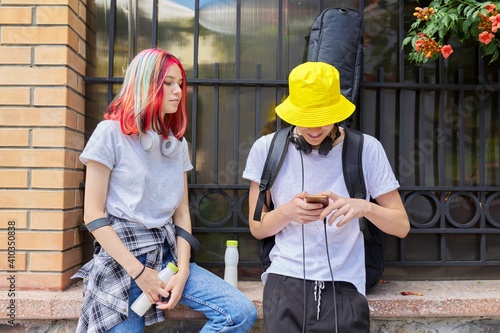 Couple of trending teenagers friends with smartphone on city street