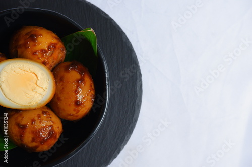 boiled eggs cooked in soy sauce in a black bowl in white background