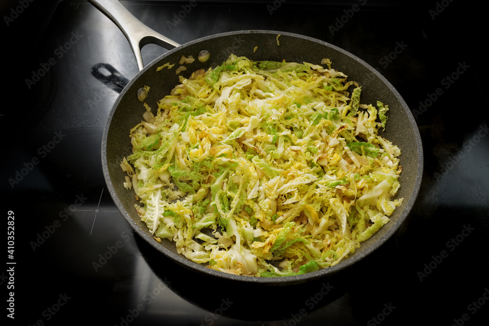 Savoy cabbage in a frying pan on the black stove, cooking at home with healthy winter vegetables Savoy cabbage in a frying pan on the black stove, cooking at home with healthy winter vegetables