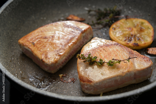 Two Tuna steaks frying in a pan with thyme and lemon for a healthy fish meal, copy space
