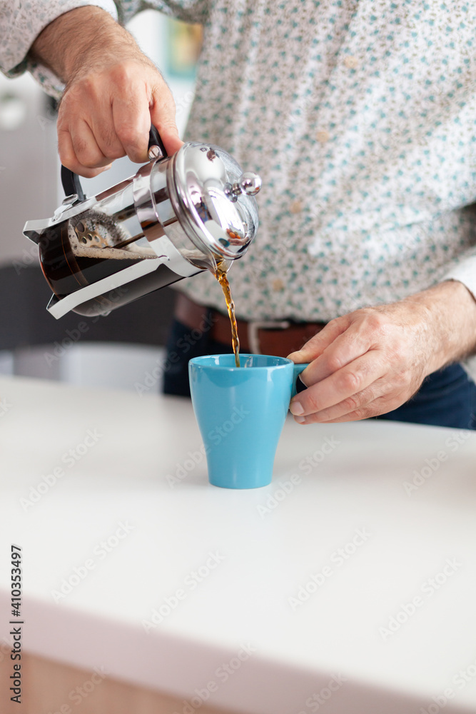 Elderly man making coffee using french press during breakfast in kitchen and pouring it in blue cup. Old person in the morning enjoying fresh brown cafe espresso cup caffeine, filter relax refreshment - obrazy, fototapety, plakaty 