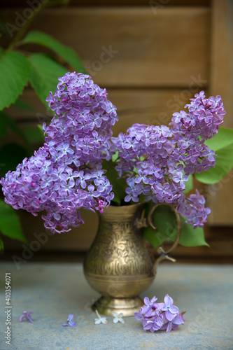 A beautiful little bouquet of lilacs on a wooden background in a brass vase. Selective focus.