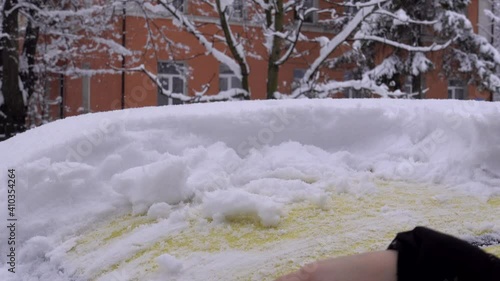 A young caucasian girl is cleaning snow from her car