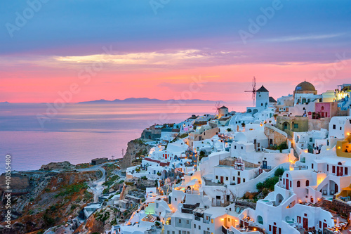 Famous greek iconic selfie spot tourist destination Oia village with traditional white houses and windmills in Santorini island on sunset in twilight, Greece