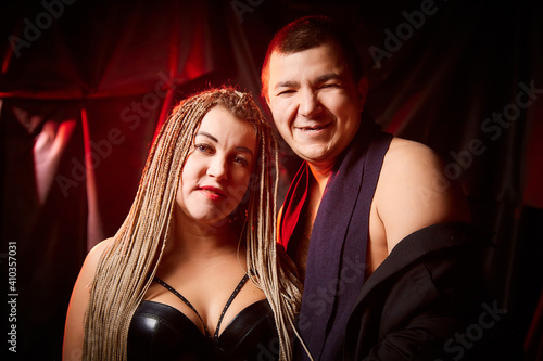 A funny cute couple of man and a plump girl with long pigtails posing in dark studio. Boy and Girl in love and black background