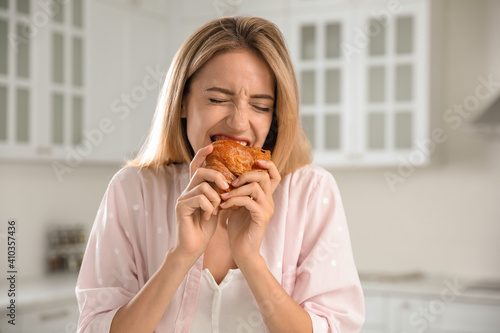 Concept of choice between healthy and junk food. Woman eating croissant in kitchen