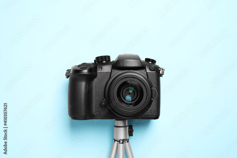 Modern camera with mini tripod on light blue background, flat lay. Video production equipment