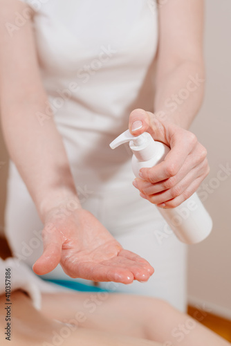 The masseuse pours massage oil into her palm. Massage room.