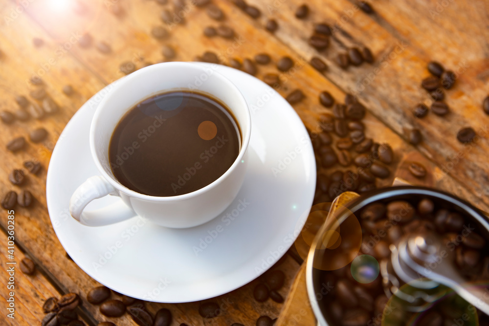 Fototapeta premium Coffee in a white cup and the grinding coffee beans place on the old wooden table. Aromatic morning coffee.