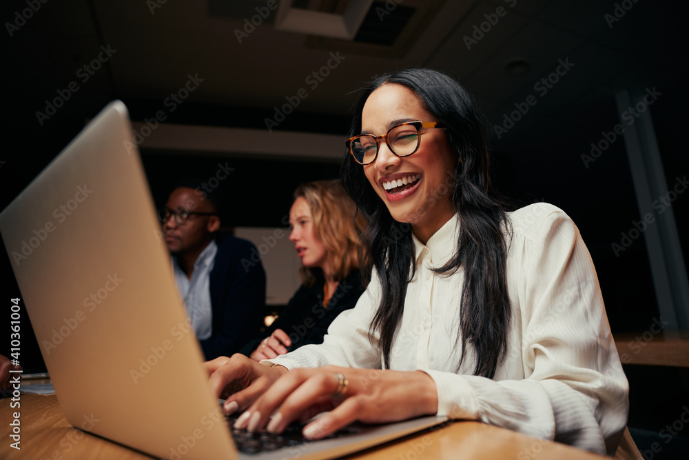 Close-up of successful smiling young African American businesswoman sitting near coworkers using laptop in office - obrazy, fototapety, plakaty 