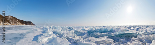 Panorama of the ice hummock field on the frozen Lake Baikal. Piles of snow-covered debris of blue ice on a sunny frosty day. Beautiful unusual winter landscape. Natural background, banner