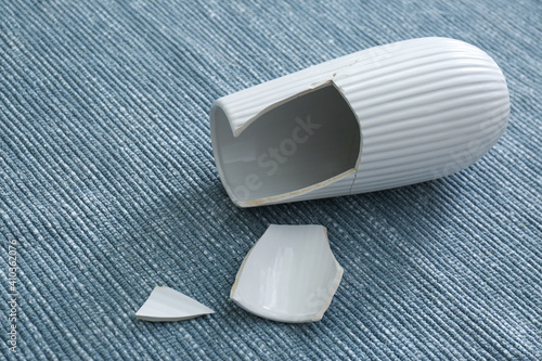 Photography Broken white ceramic vase on grey carpet, closeup