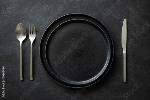 Empty black plates with silver cutlery on the black table. Top view.