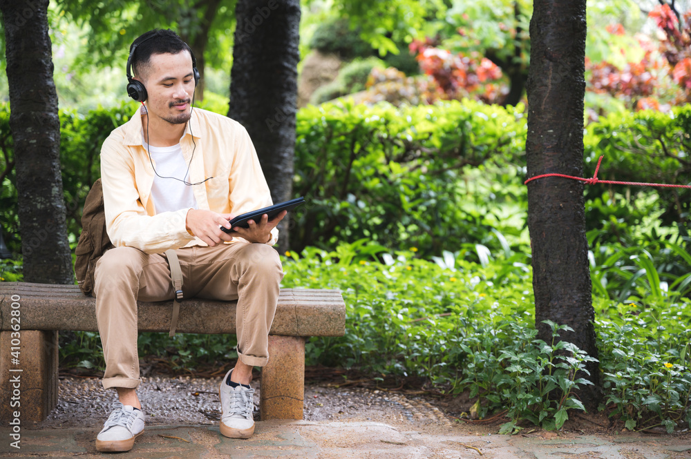 A young asian man chilling and relaxing by listen to music with headphone in the park. Good feeling of the sunny day at the garden in the vacation leisure time. A young asian man chilling and relaxing by listen to music with headphone in the park. Good feeling of the sunny day at the garden in the vacation leisure time.