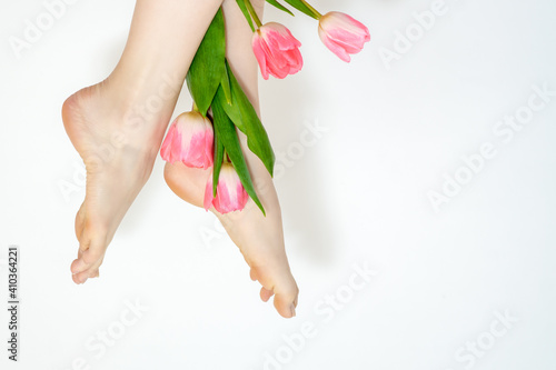 Beautiful slim smooth woman's legs with tulips flowers on white background