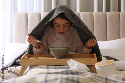 Woman with plaid doing inhalation above bowl on bed