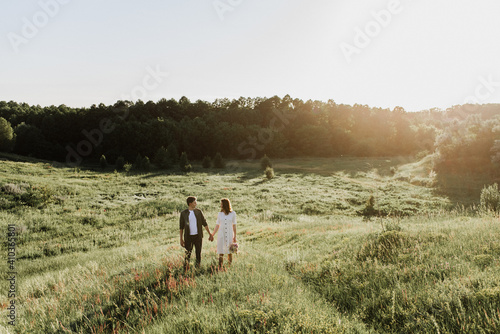 Fototapeta Naklejka Na Ścianę i Meble -  Young beautiful woman and man hug, kiss and walk in nature at sunset.