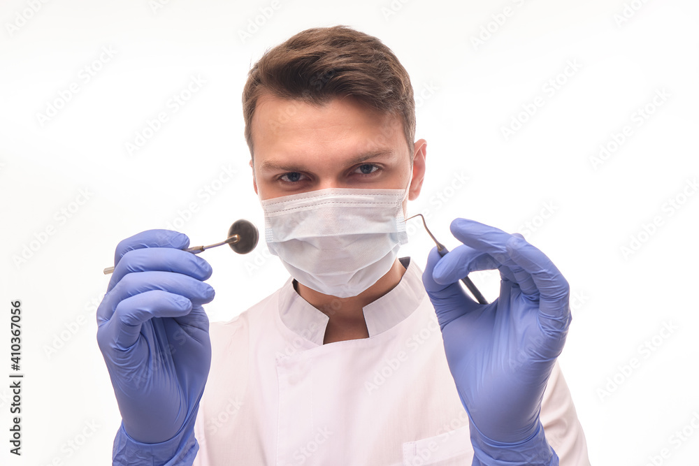 Doctor close-up on a white isolated background. The doctor holds dental instruments in his hands to examine the patient Doctor close-up on a white isolated background. The doctor holds dental instruments in his hands to examine the patient