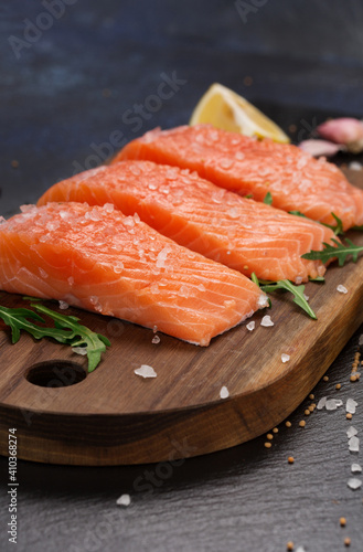 Raw fillet of salmon with sea salt, lemon and pepper on black stone background.