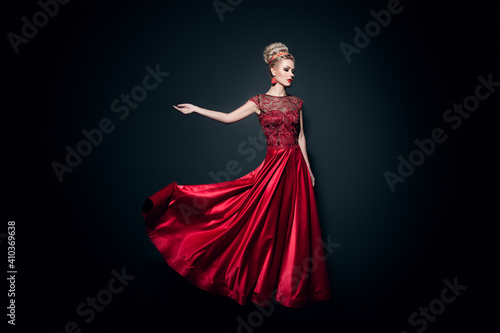 Fulll length image of a wonderful young woman dressd in a long fluing red dress with raised hand, over black background.