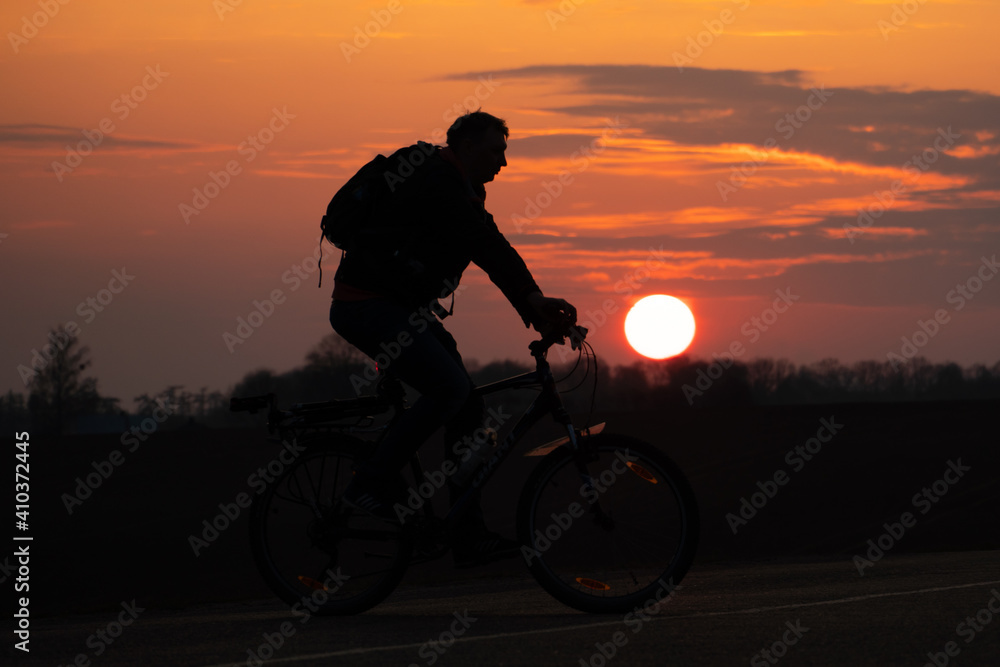 Obraz premium The silhouette of a cyclist against the background of the sun and the beautiful sky. The outline of a man riding on a bicycle against the background of the sunset.