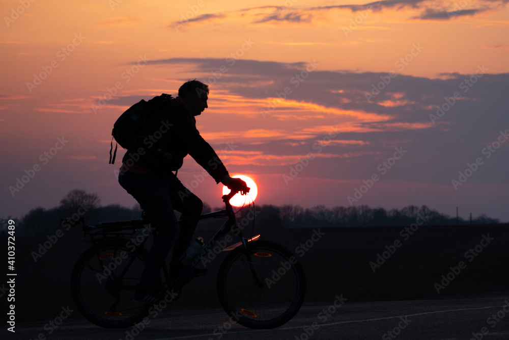 Obraz premium The silhouette of a cyclist against the background of the sun and the beautiful sky. The outline of a man riding on a bicycle against the background of the sunset.