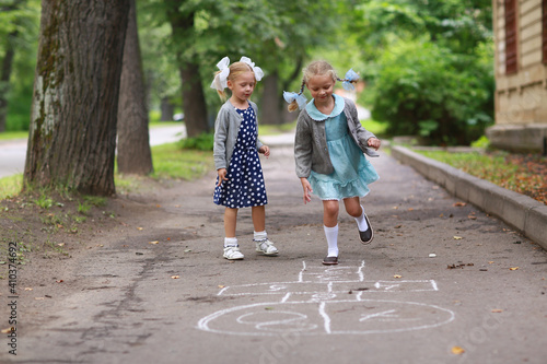 Two little girlfriends in blue dress and pigtails on her head playing hopscotch in the yard