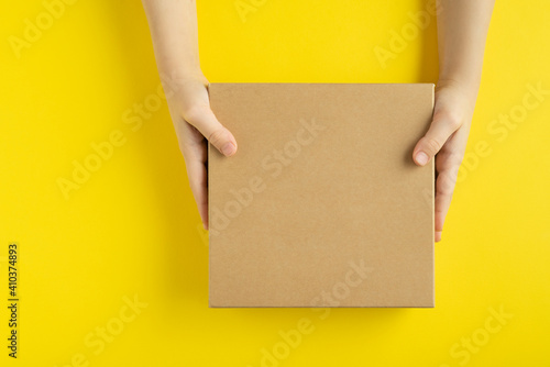 Craft box in hands on yellow background, top view. Copy space. Mock up.