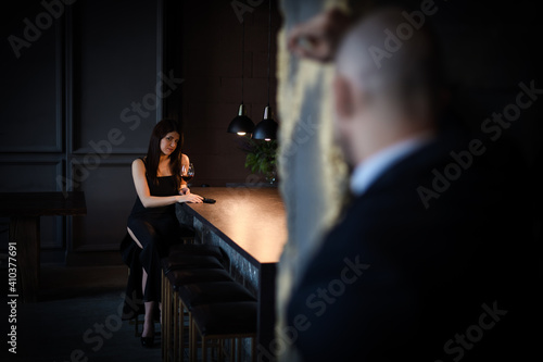 A man and a woman, stills from the film. A beautiful brunette in a black dress is sitting at the bar drinking wine and a gun is lying next to her, a bald man is looking at her. Valentine's Day