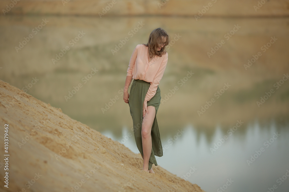 cheerful girl in a dress dancing in the sand at the lake