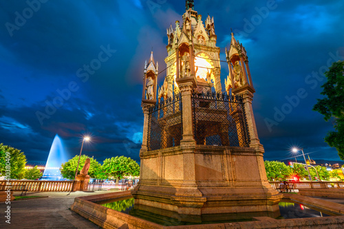 Brunswick Monument in Jardin des Alpes, a mausoleum built in 1879. Jet d'eau fountain, sybol of the city, in Lake Leman on the background. Geneva in French-Swiss, Switzerland. Urban cityscape by night photo