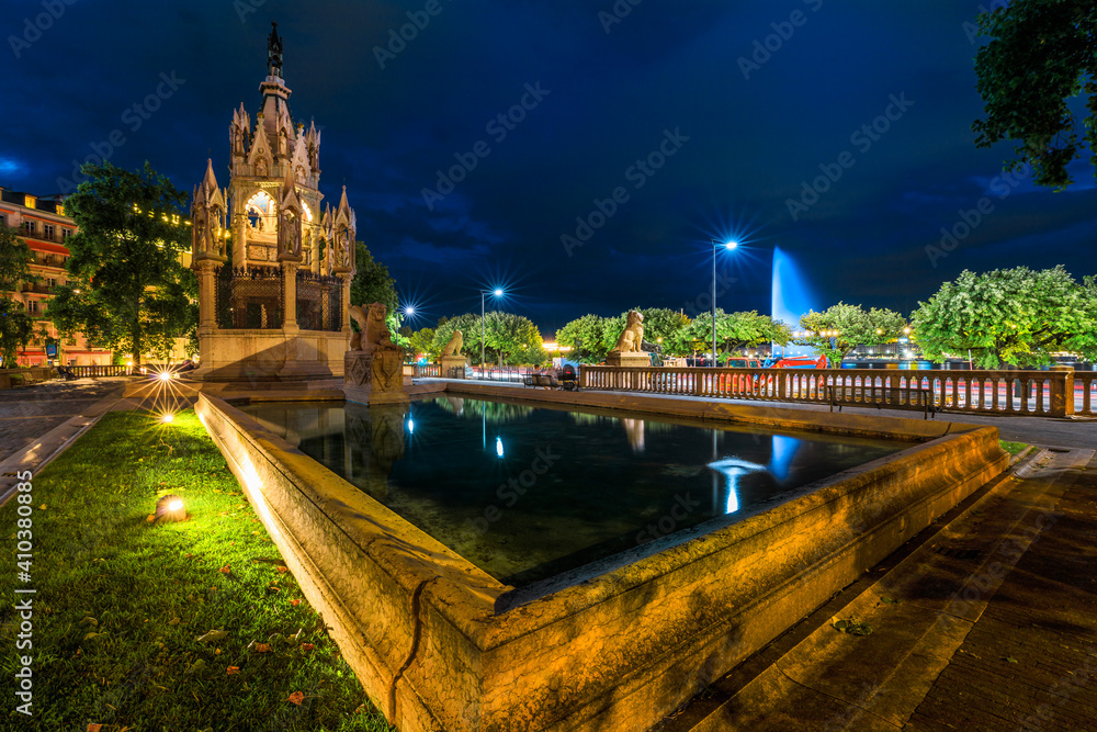 Brunswick Monument with Lion statue in Jardin des Alpes, a mausoleum built in 1879. Jet d'eau, sybol of city, and Lake Leman, reflecting in water fountain. Geneva, French-Swiss in Switzerland by night