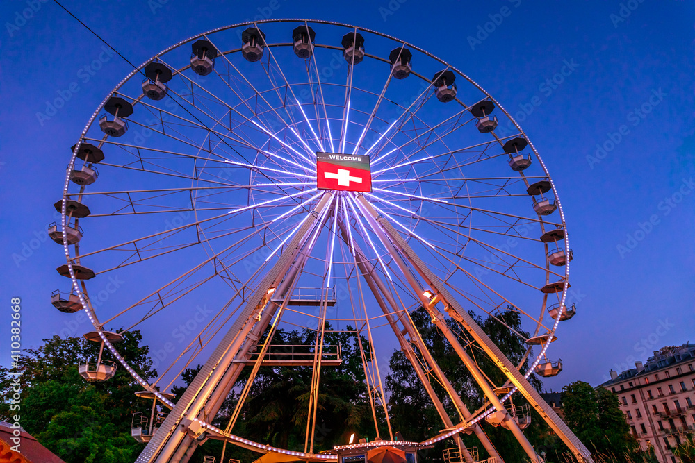 Bottom view of Swiss Ferris Wheel with flag of switzerland by night. Night view of Geneva cityscape in French Swiss, Switzerland. Bottom view of Swiss Ferris Wheel with flag of switzerland by night. Night view of Geneva cityscape in French Swiss, Switzerland.