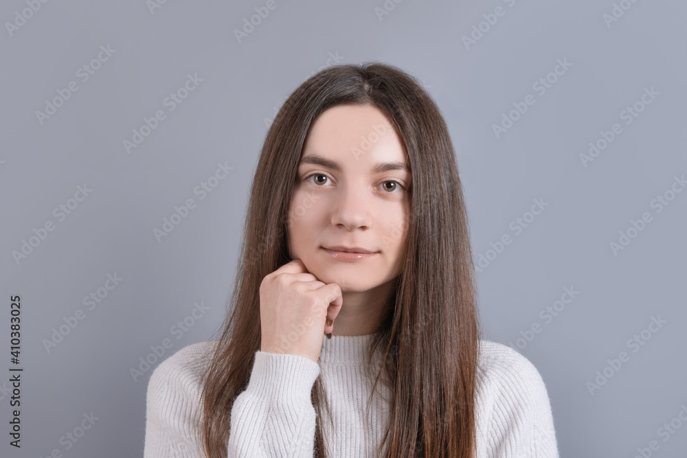 Portrait of a young attractive girl woman with dark long hair easily smiling on a gray studio background. Place for text. With copy space Portrait of a young attractive girl woman with dark long hair easily smiling on a gray studio background. Place for text. With copy space
