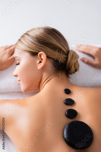 Woman with closed eyes getting hot stone massage near burning candle in spa salon