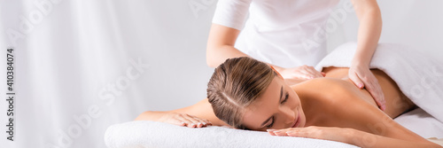 masseur massaging pleased young woman on massage table in spa salon, banner