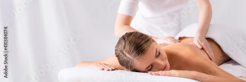 Obraz masseur massaging pleased young woman on massage table in spa salon, banner