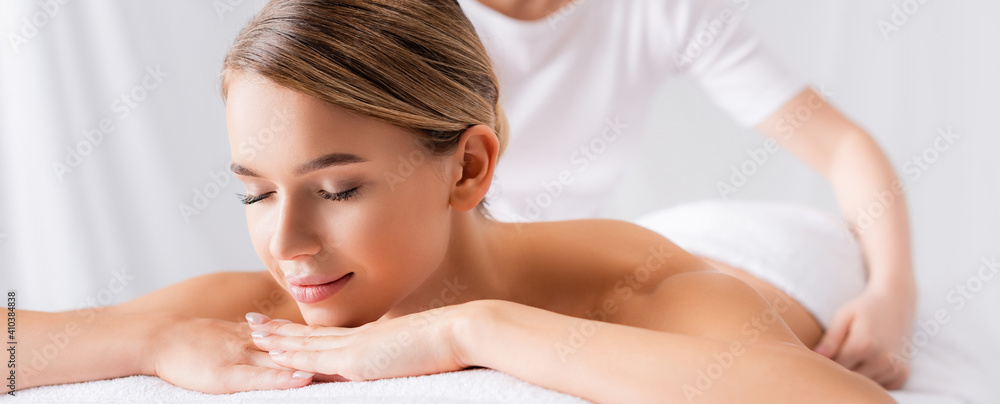Young woman lying on massage table near masseur on blurred background, banner - obrazy, fototapety, plakaty 