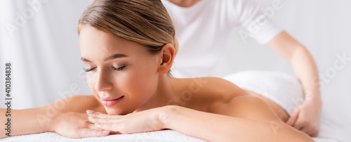 Young woman lying on massage table near masseur on blurred background, banner